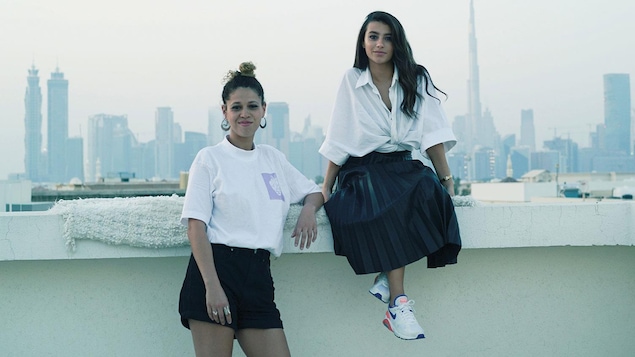 Photo de deux jeunes femmes qui posent devant le paysage d'une ville qui se dessine derrière elles.
