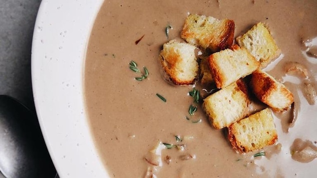 Photo d'une crème aux champignons servie dans une assiette avec des croûtons et du thym.