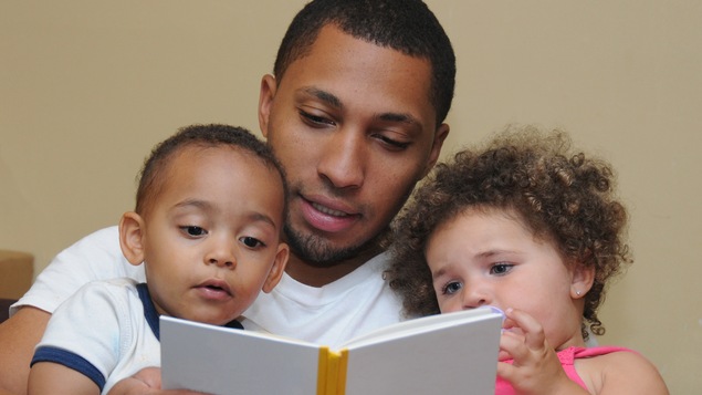 Un père immigrant fait la lecture à ses deux enfants. Le rôle de père est différent d'une culture à l'autre.