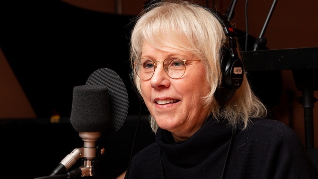 La femme aux cheveux blonds et aux lunettes rondes sourit à l'animatrice.