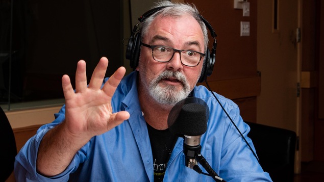 Le comédien à lunettes gesticule en parlant.