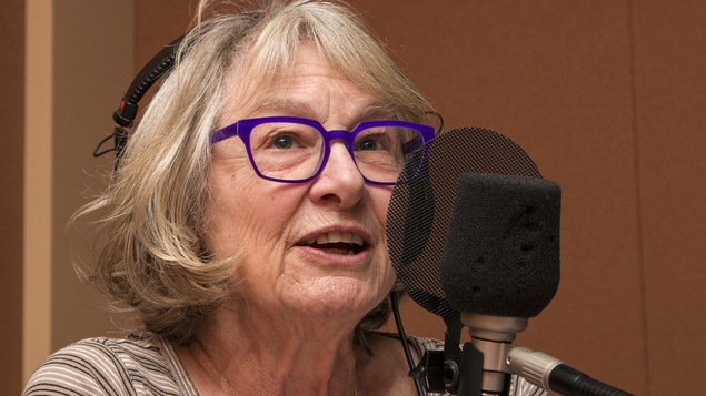 Affublée de lunettes bleues, la comédienne parle au micro.