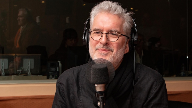 L'animateur et auteur, tout de noir vêtu, sourit à l'animatrice.