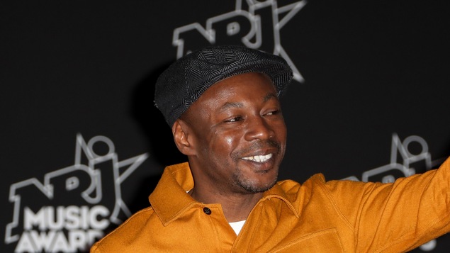 MC Solaar aux NRJ Music Awards le 4 novembre 2017 au Palais des Festivals, à Cannes. Portant une chemise jaune éclatante, il sourit aux caméras en brandissant un pouce en signe d'approbation.
