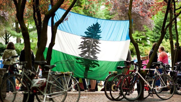 Le drapeau de la république de Cascadia accroché à deux arbres lors d'un rassemblement.