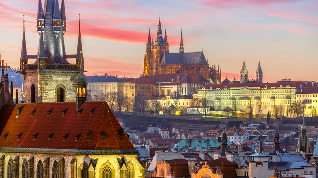 Vue aérienne de la ville de Prague avec la lumière chaude d'un coucher de soleil. On voit une église médiévale en avant plan.
