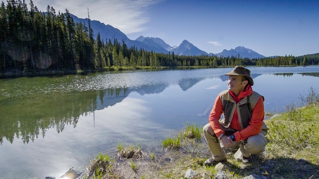 Arthur l'aventurier, accroupit près d'un plan d'eau, contemple la beauté des Rocheuses