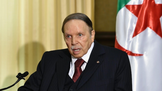 Abdelaziz Bouteflika assis devant un micro, un drapeau algérien derrière lui.