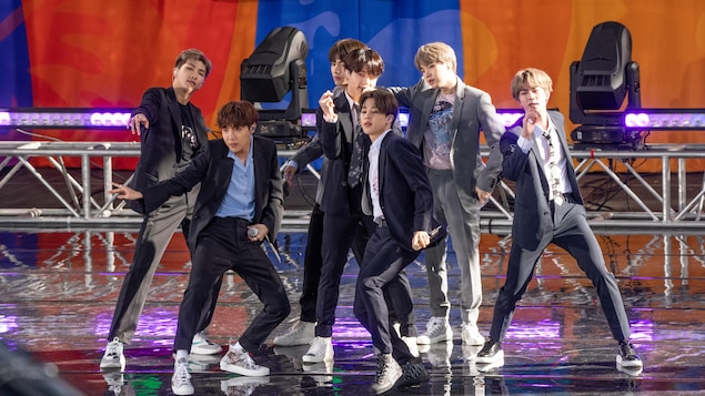 Les membres du groupe BTS dansent et chantent sur une scène.