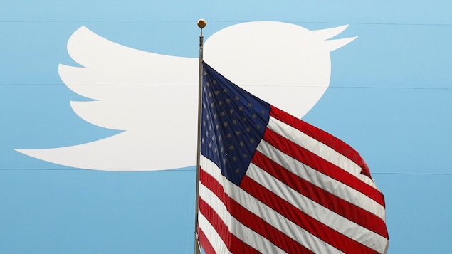Le logo du réseau social Twitter est placé derrière un drapeau des États-Unis.