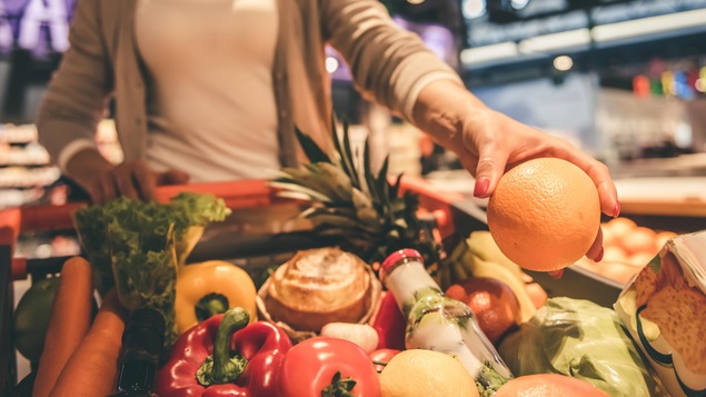 Une femme pousse un panier d'épicerie rempli de légumes et de fruits.