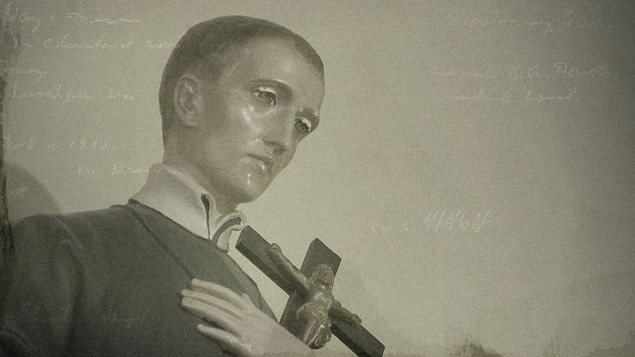 Plan rapproché d'une statuette en bois représentant un curé, avec une crucifix à la main.