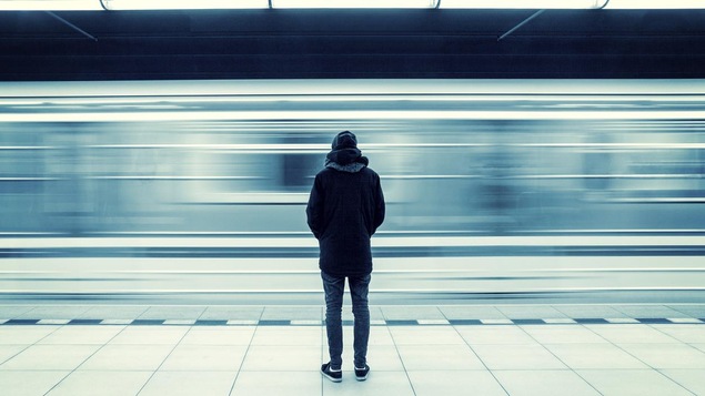 L'homme habillé chaudement est immobile. Il regarde passer le métro, flou.
