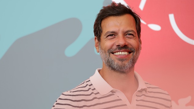 Laurent Lafitte souriant sur un fond rouge et bleu.