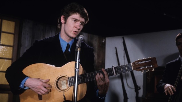 Robert Charlebois guitare à la main dans un studio.