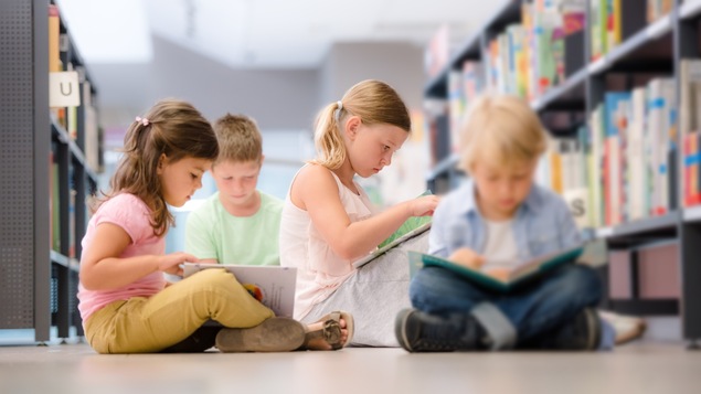 Quatre enfants lisent des livres assis par terre dans une bibliothèque