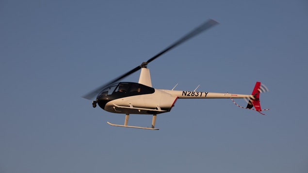 Un hélicoptère blanc vol dans les airs sous un ciel bleu.