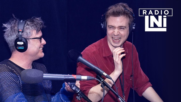 Photo de Stéphane Archambault et Arnaud Soly qui rigolent devant des micros de radio.
