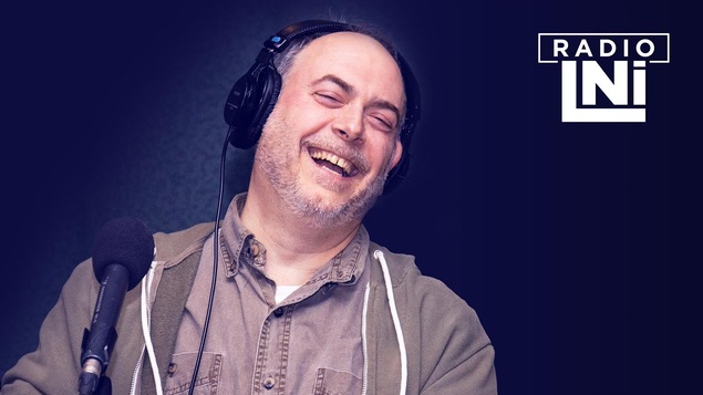 Photo de Martin Héroux, en train de rire, devant un micro de radio.