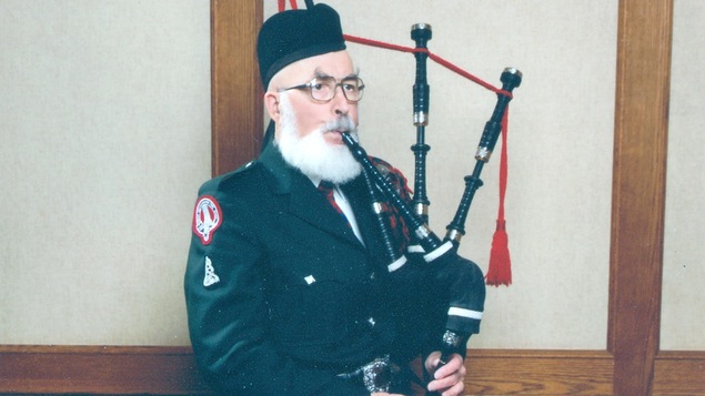 Un homme avec une barbe blanche en habit traditionnel écossais qui joue de la cornemuse
