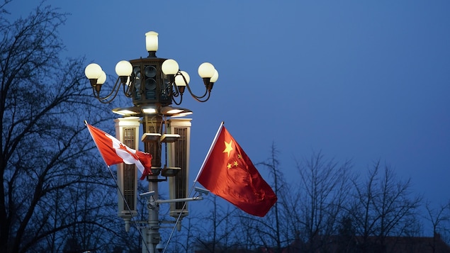 Le soir, un drapeau du Canada et un drapeau de la Chine flottent côte à côte sur un lampadaire allumé.