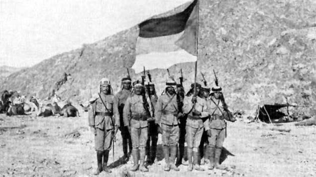 Des soldats dans le désert tiennent un drapeau.