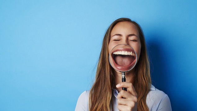 une femme qui rit, elle tient une loupe qui accentue son rire