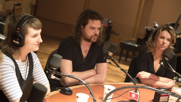 Trois personnes assises à une seule table ronde, sur laquelle se trouve des micros.