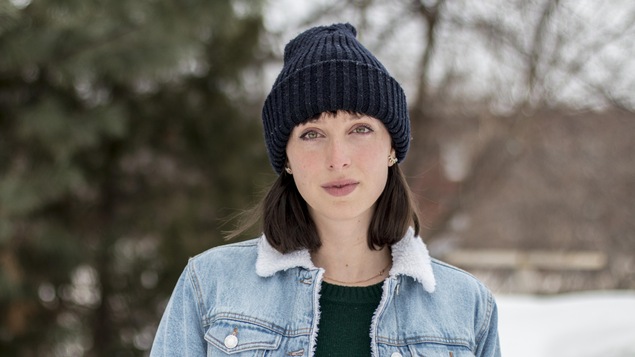 Elle porte une tuque bleue et un veston en jeans.