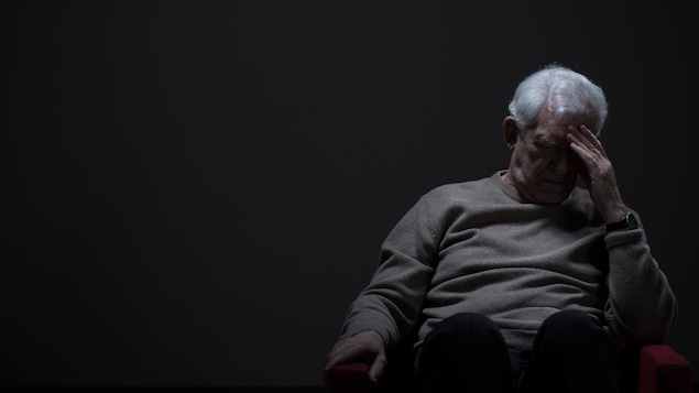 Un homme qui déprime devant un mur gris.