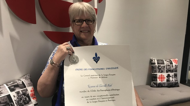 Une femme tient un document officiel devant un logo de Radio-Canada
