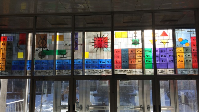 Un vitrail avec les éléments du tableau périodique de différente couleurs.