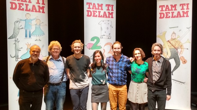 Les 7 membres du groupe Tam di delam debout devant des affiches où on peut voir des dessins d'enfantins.