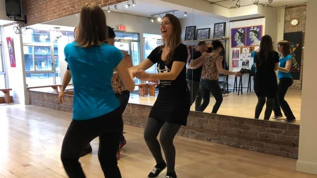 Dans un studio de danse, devant un mur miroir, des danseurs pratiquent le swing