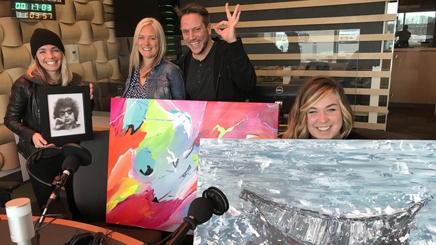 Trois femmes et un homme tenant trois toiles tout en souriant dans le studio F de Radio-Canada Acadie