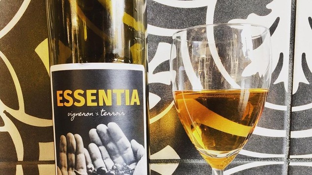 Une bouteille de vin orange Essentia, avec une coupe juste à côté.