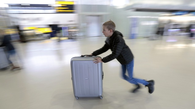 Un enfant pousse sa valise sur roues dans un aéroport.