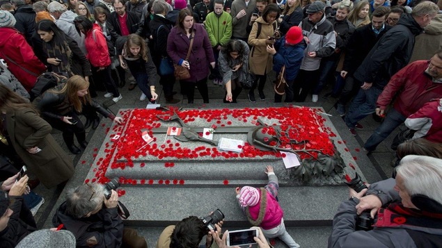 Des gens déposent des coquelicots rouge sur la tombe du soldat inconnu au Monument commémoratif de guerre du Canada lors du jour du Souvenir à Ottawa en 2015. Un enfant monte sur la tombe.