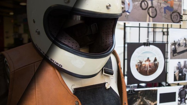Un mannequin porte un casque de moto, une salopette et une veste sans manche en cuir.