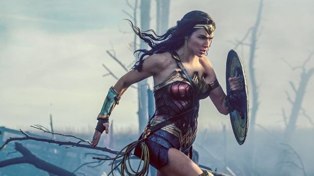 L'actrice Gal Gadot dans le costume de Wonder Woman, court dans une forêt enfumée, bouclier sur la bras gauche.