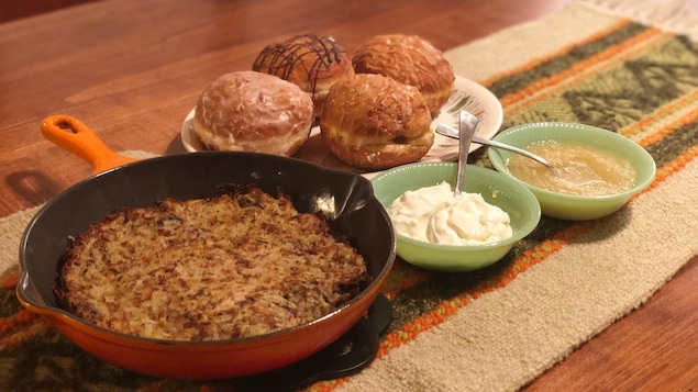 Une table avec une latke géante, des beignets soufganiyot, de la crème sûre et de la compote de pommes.