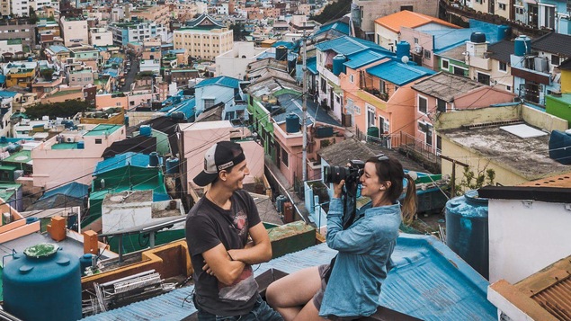 Alex Normand et MJ Lalande, d'Alex & MJ On the Go posent pour une photo avec les toits de la ville de Busan, en Corée du Sud en arrière-plan.