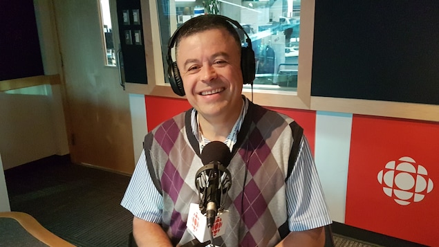 Un homme est assis dans un studio radio, devant un microphone.