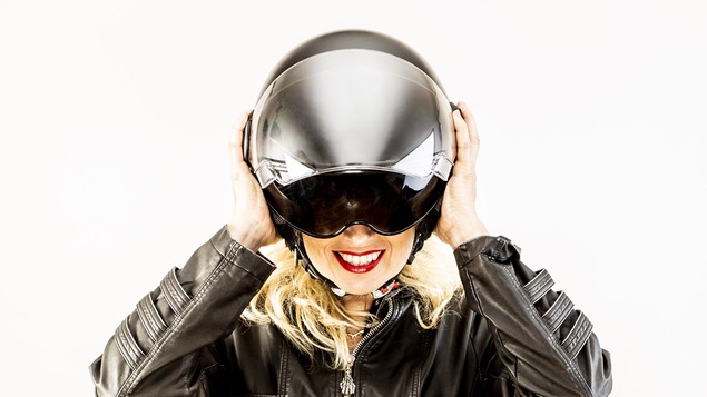 Plan taille d'une femme aux cheveux blonds qui ajuste sur sa tête un casque de moto.