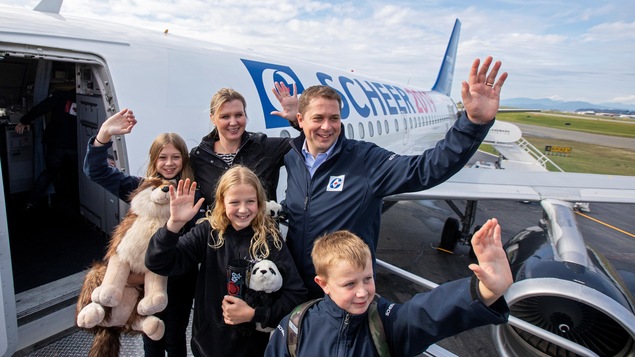 Un couple et trois enfants saluent la foule à la porte d'entrée d'un avion.