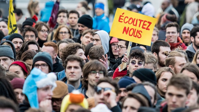 Une foule de protestataires dont l'un tient une pancarte sur laquelle il est écrit «Écoutez-nous».