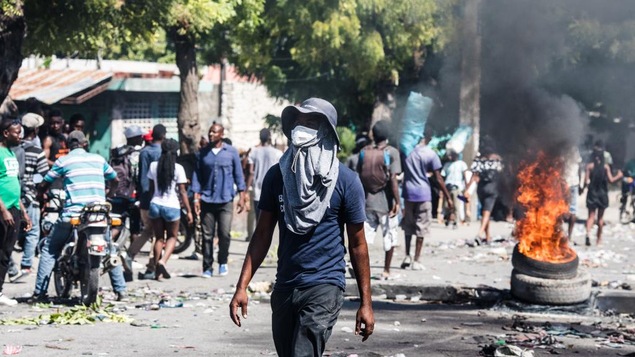 Des pneus en feu dans les rues de Port-au-Prince, à côté de déchets et de gens qui marchent.