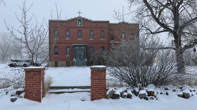 Image du couvent sous la neige. Le couvent a une croix sur le toit et une grande porte d'entrée verte.