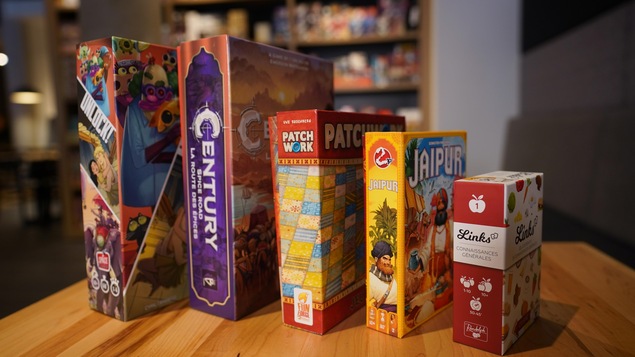 Cinq boîtes de jeux de société posées sur une table.