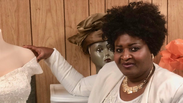 Leonnie debout à côté d'une robe de mariage qu'elle a créée